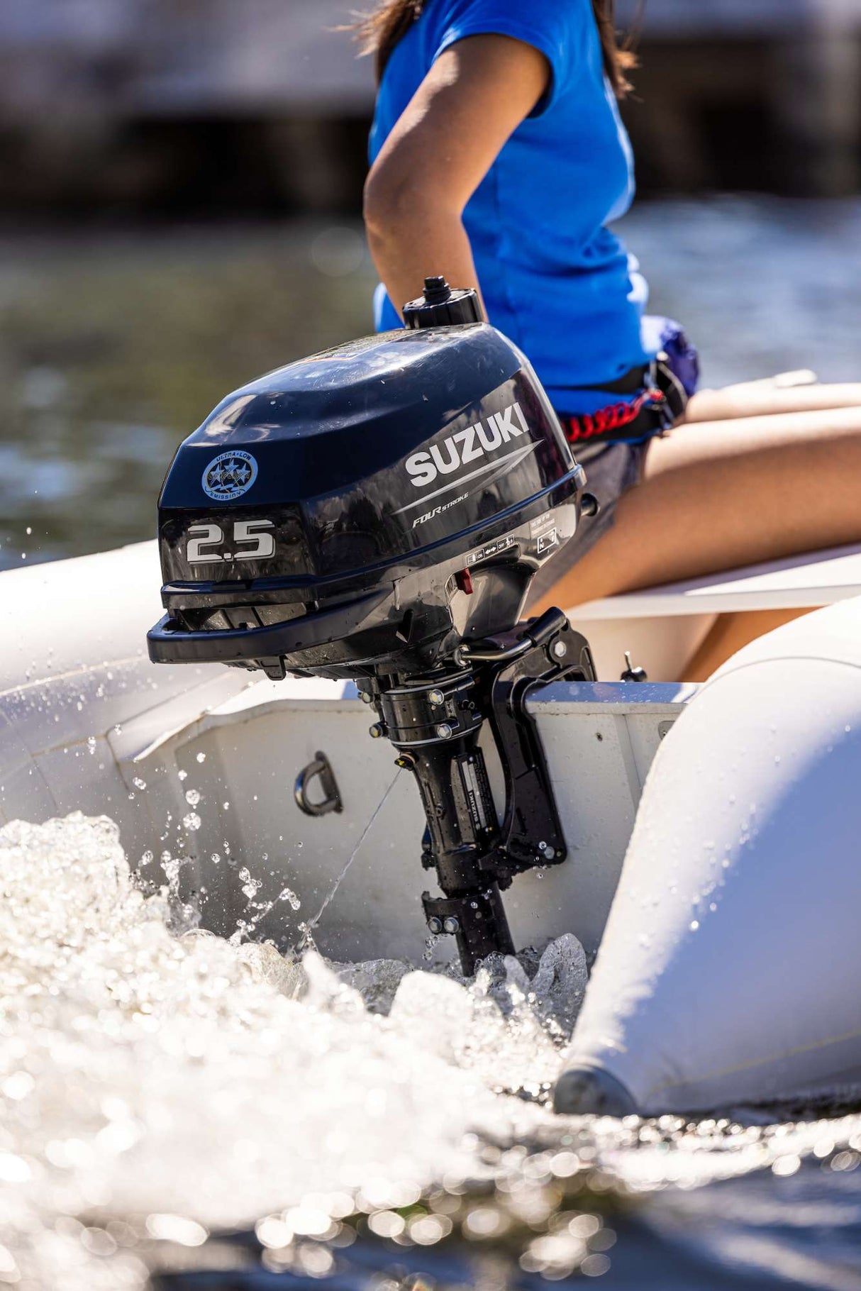 Woman operating a white inflatable boat powered by a Suzuki 2.5 HP outboard motor on sunny open water.