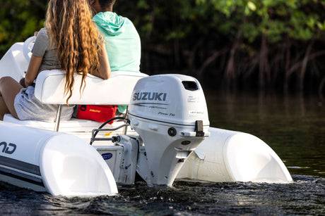 Couple riding an inflatable boat powered by a white Suzuki 20 HP outboard motor with Lean Burn technology.