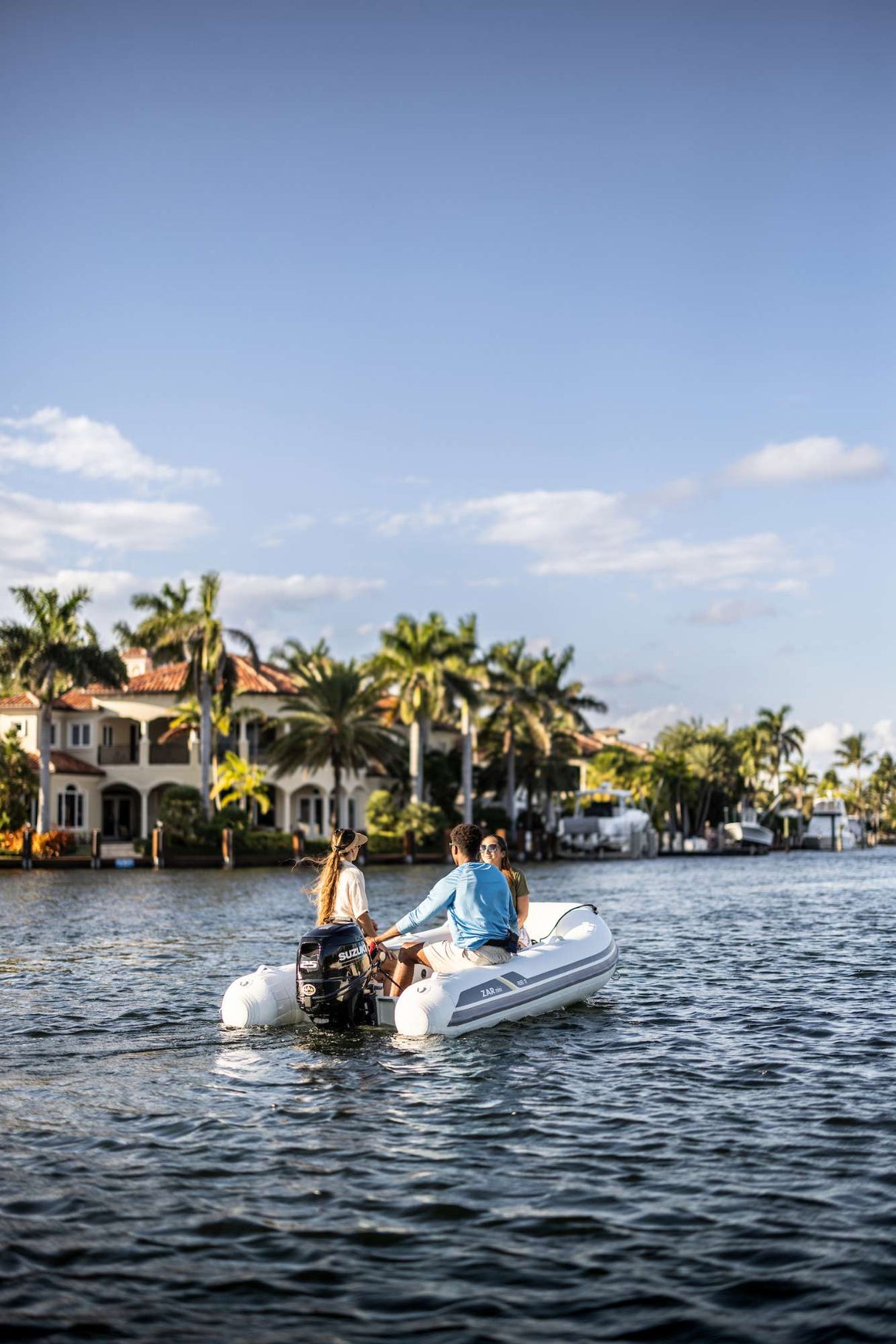 Group cruising a Florida canal on a Mini inflatable boat with a Suzuki 25 HP outboard motor, passing waterfront homes.