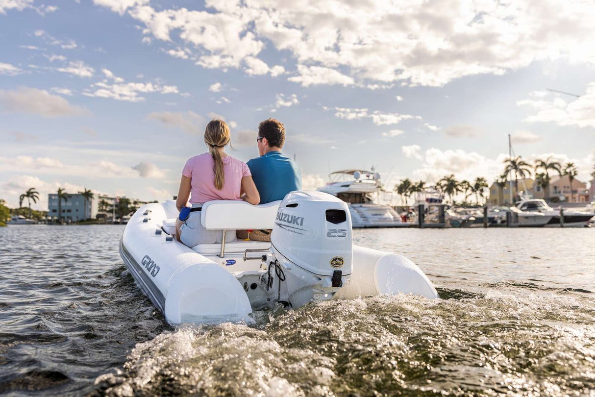 Inflatable boat with Suzuki 25 HP outboard motor near marina on sunny day.