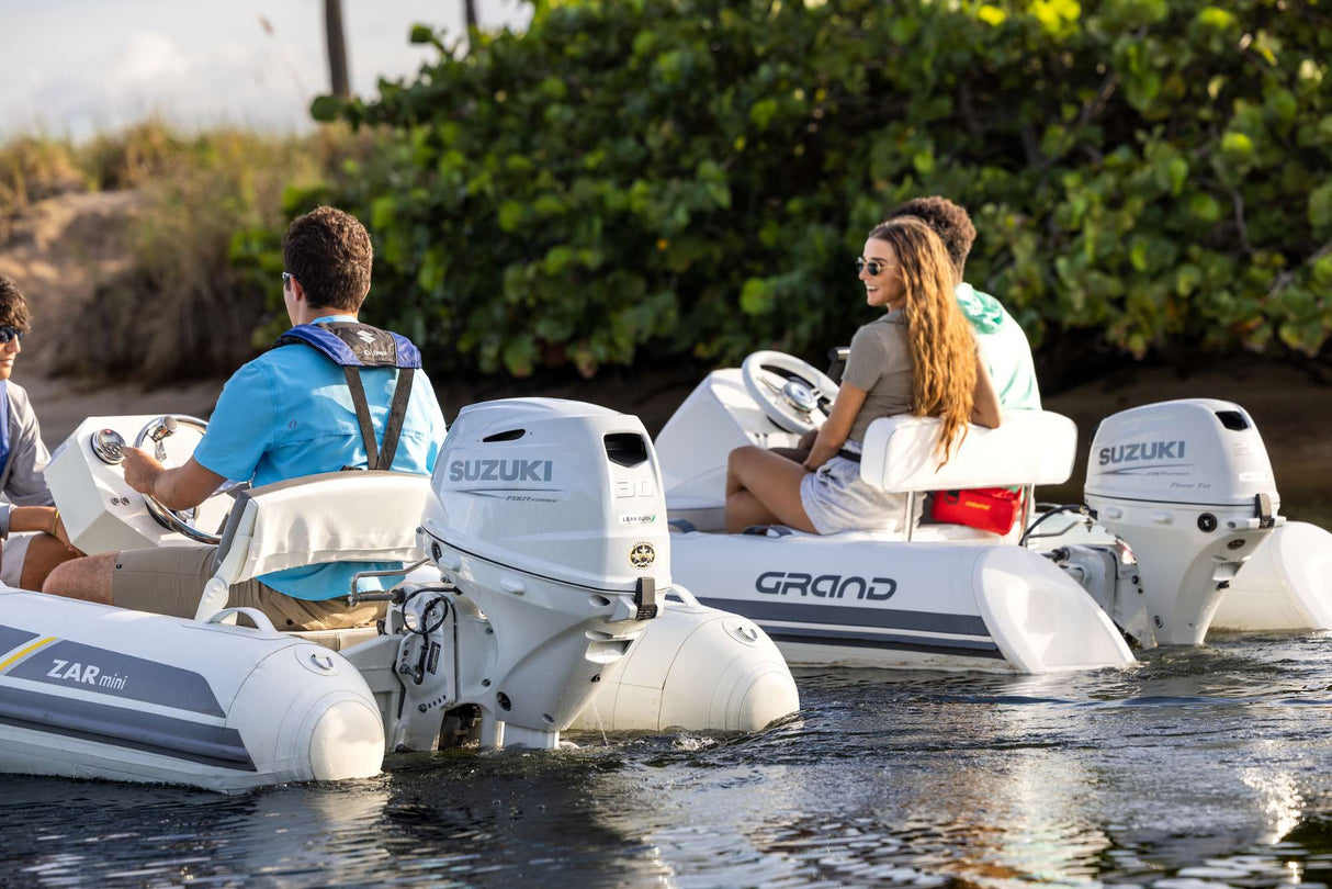 Suzuki 30 HP and 20 HP outboard motors powering inflatable boats near a shoreline with greenery.