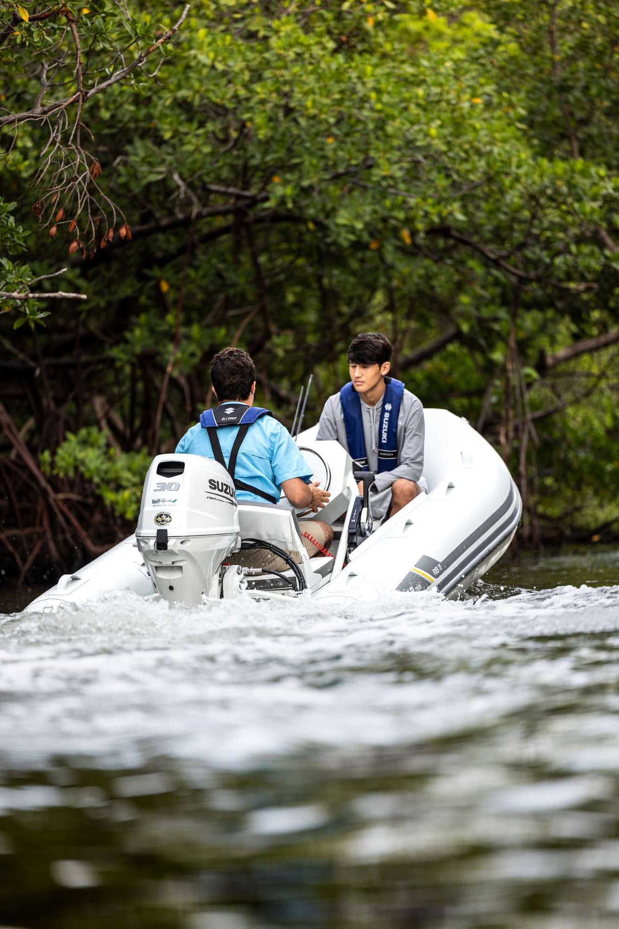 Two men cruising through mangroves on a white inflatable boat powered by a Suzuki 30 HP outboard motor.