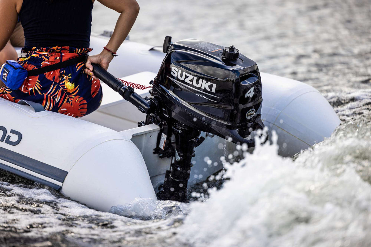 Person driving an inflatable boat powered by a black Suzuki 4 HP four-stroke outboard motor through choppy water.