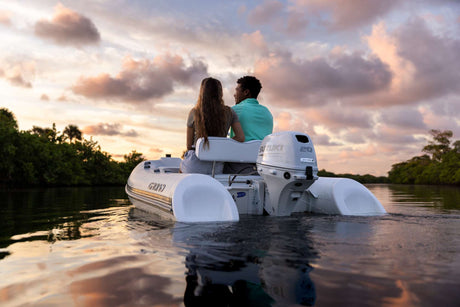 Couple cruising on a white inflatable boat powered by a Suzuki 20 HP four-stroke outboard motor during a peaceful sunset on calm water.