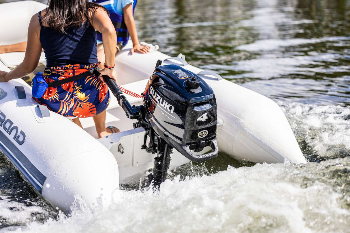 Suzuki 4 HP outboard motor with tiller handle mounted on an inflatable boat underway on calm water.