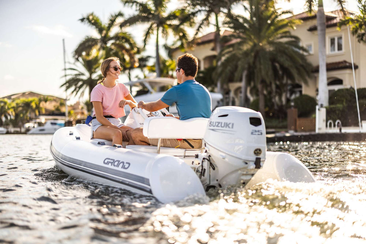 Suzuki 25 HP outboard motor powering a Grand inflatable boat near waterfront homes in sunny weather.