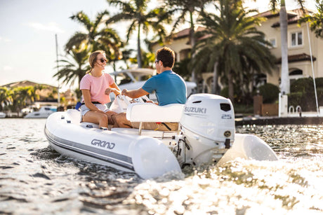 Suzuki 25 HP outboard motor powering a Grand inflatable boat near waterfront homes in sunny weather.